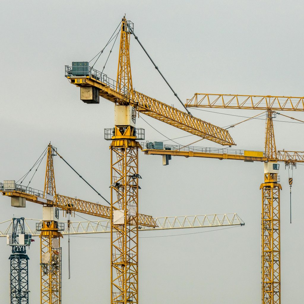 Multiple yellow tower cranes against a gloomy sky, depicting industrial construction.