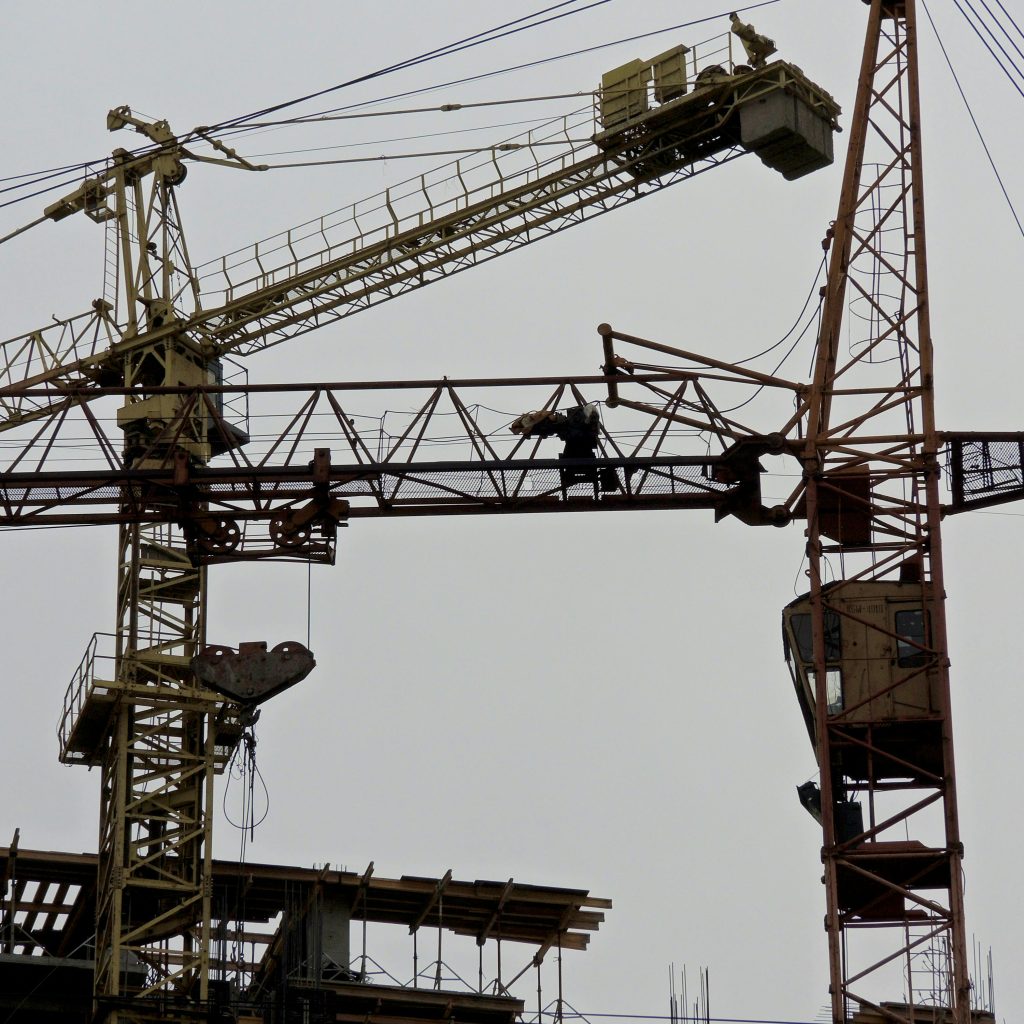 From below of metal industrial cranes located in contemporary construction site against gray sky